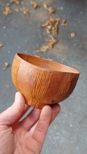 A hand holding a small, carved wooden bowl. Grooved patterns decorate the outside.